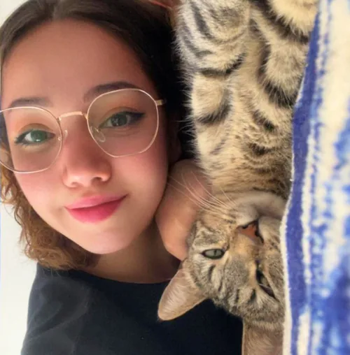 Erica lying down with her tabby cat Nina draped over her shoulder