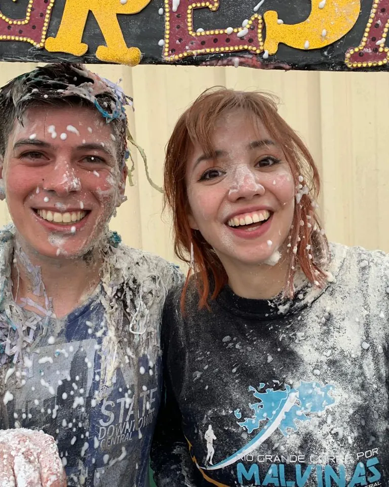 Erica and a classmate covered head to foot in foam and flour in front of a hand-painted banner