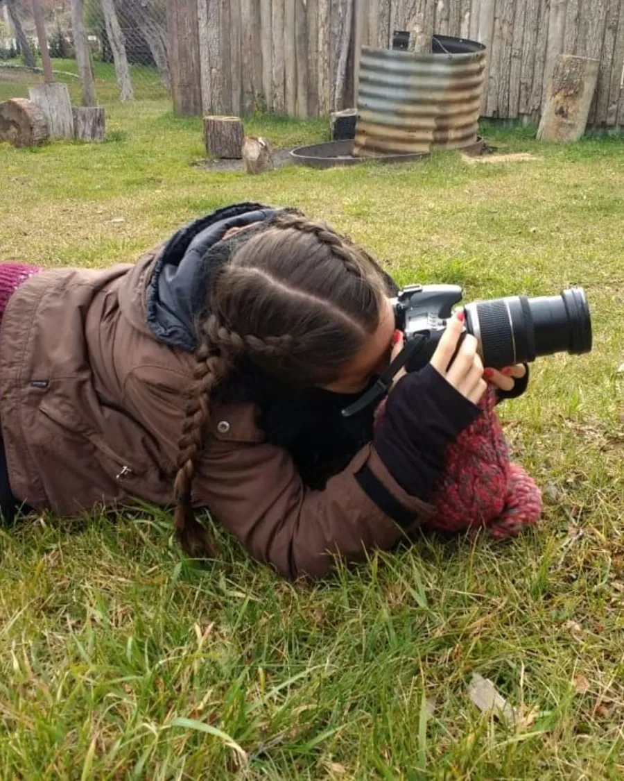 Erica flat on her stomach in the grass, shooting with a DSLR held right down at ground level