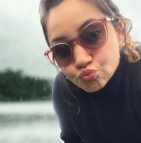 Erica in sunglasses, pulling a face, by a grey lake