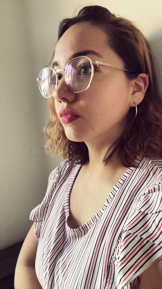 Erica in a striped blouse and round glasses, looking off to the side