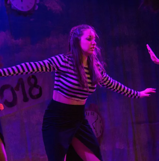 Erica in a striped top and black skirt, arms wide, under magenta light