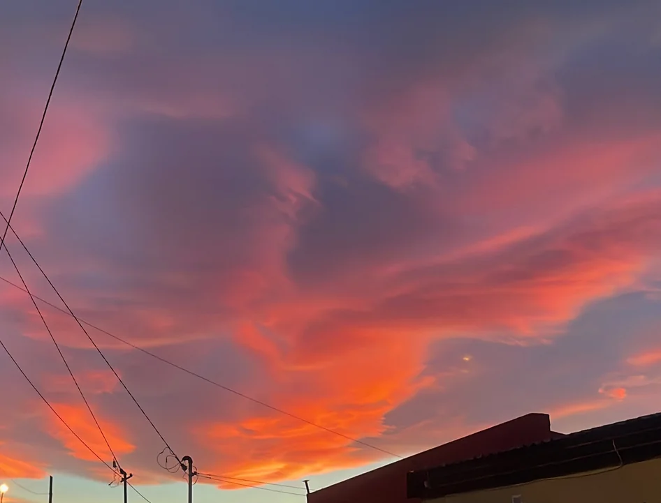 Sunset over Tierra del Fuego: violet and orange cloud spread right across the sky, power lines cutting down the left of the frame and the dark edge of a roof at the bottom.